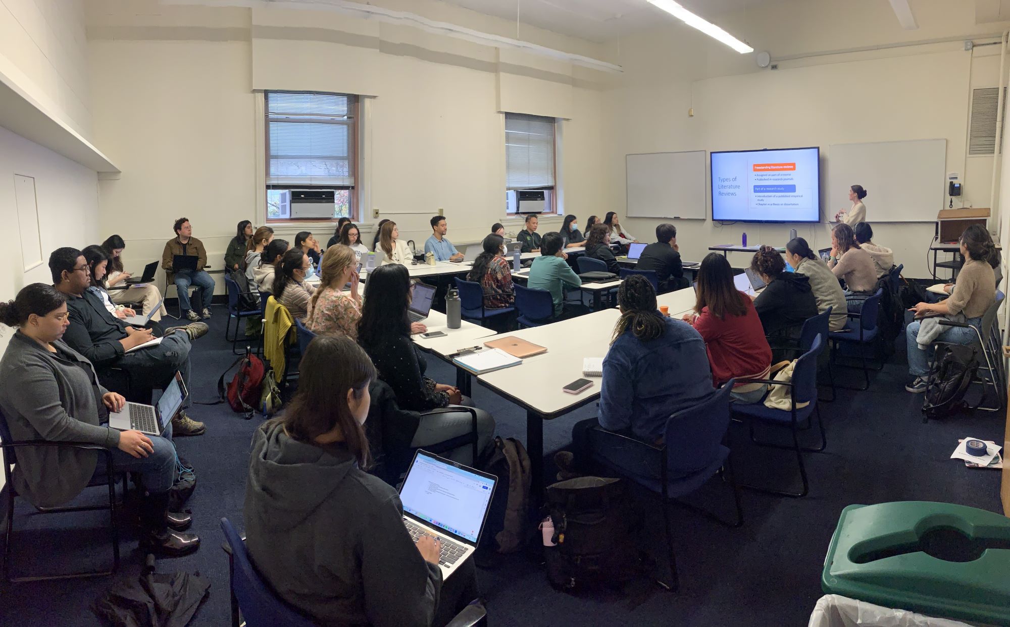 full classroom of students seated at tables with laptops facing an electronic monitor at the head of the room