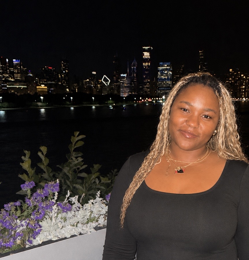 Photo of a student smiling at the camera in front of a night sky with buildings lit up