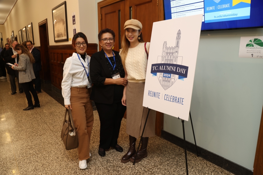 3 TC Alumni Day attendees standing next to a TC Alumni Day sign