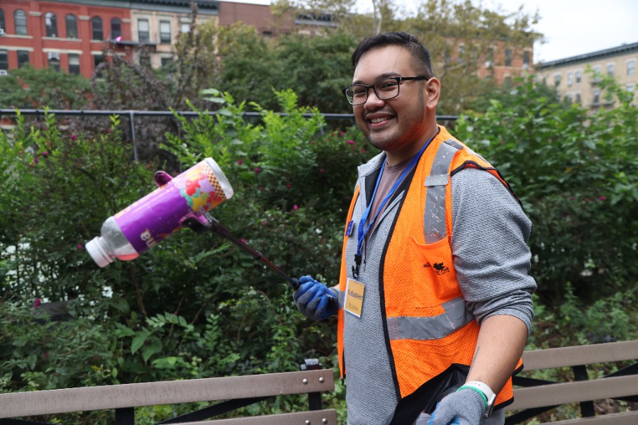 Person wearing a brightly colored vest participating in a volunteer neighborhood clean up activity holding a bottle with a trash picker tool.