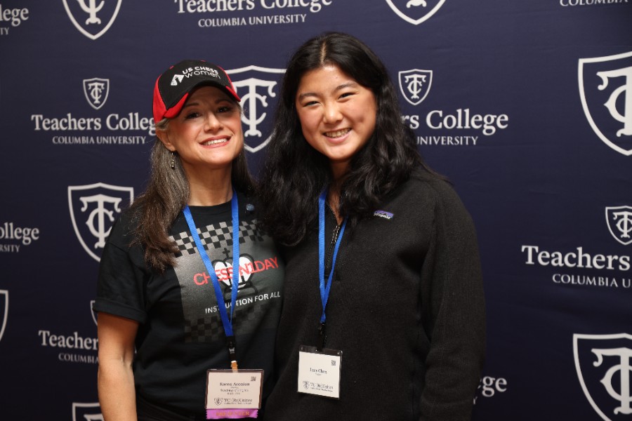 Two people wearing lanyards smiling with TC signs behind them