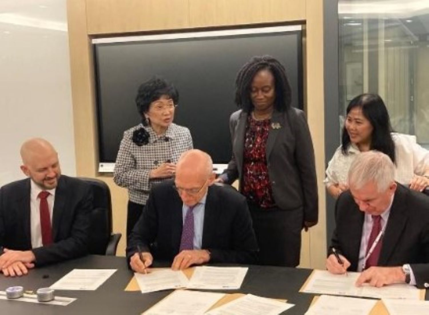 Tom Bailey and others at a signing ceremony signing documents at a desk