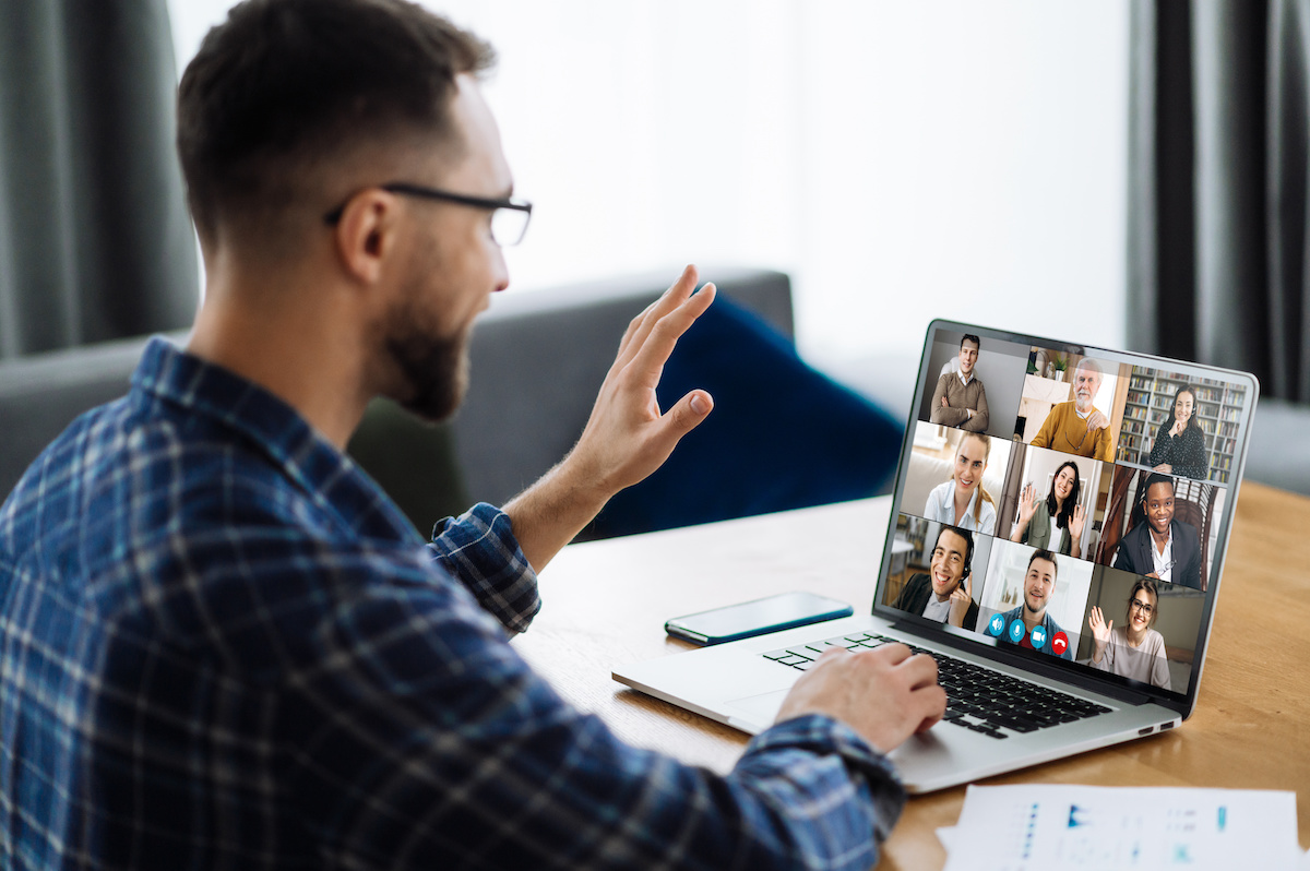 A man waving while sitting in front of a laptop on a video conference call with nine other people