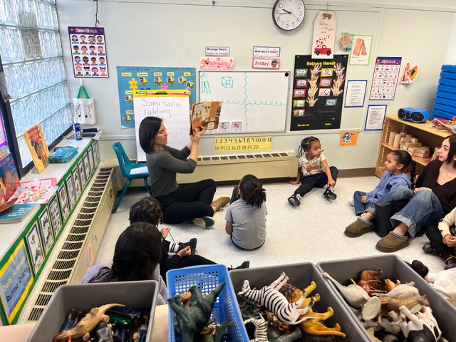 A teacher reads a book to a small group of children sitting in a circle during a classroom story time activity.