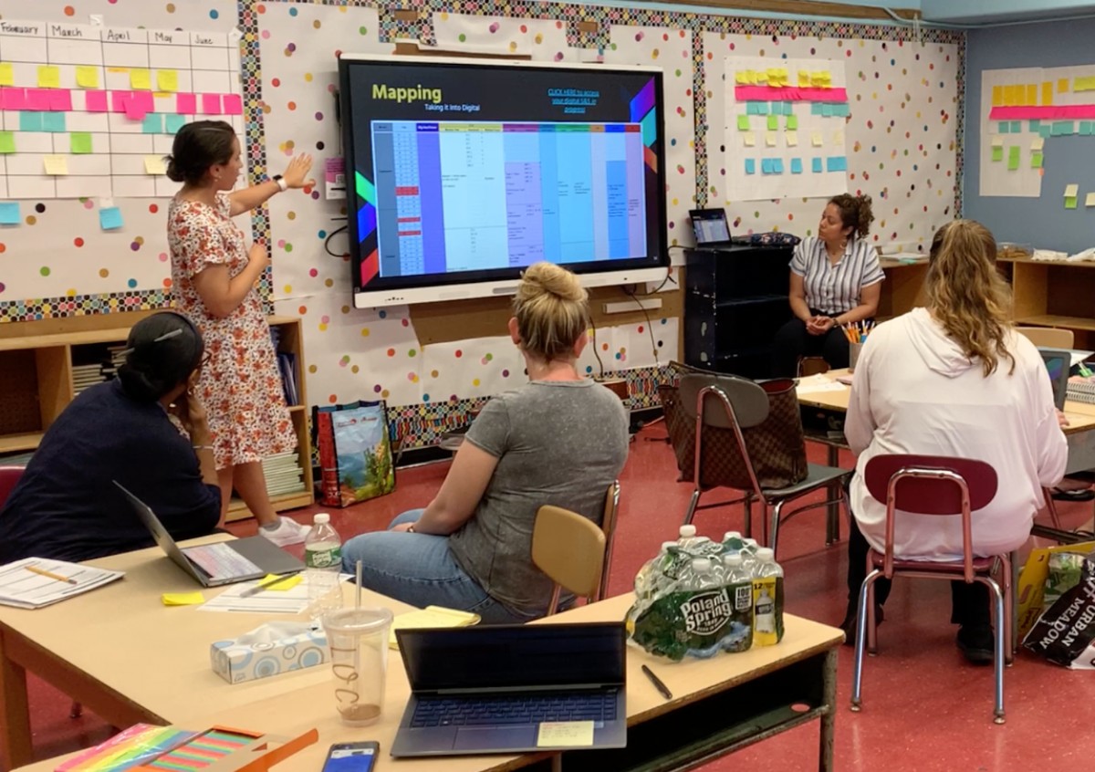 Four educators seated in a classroom setting looking at a screen together