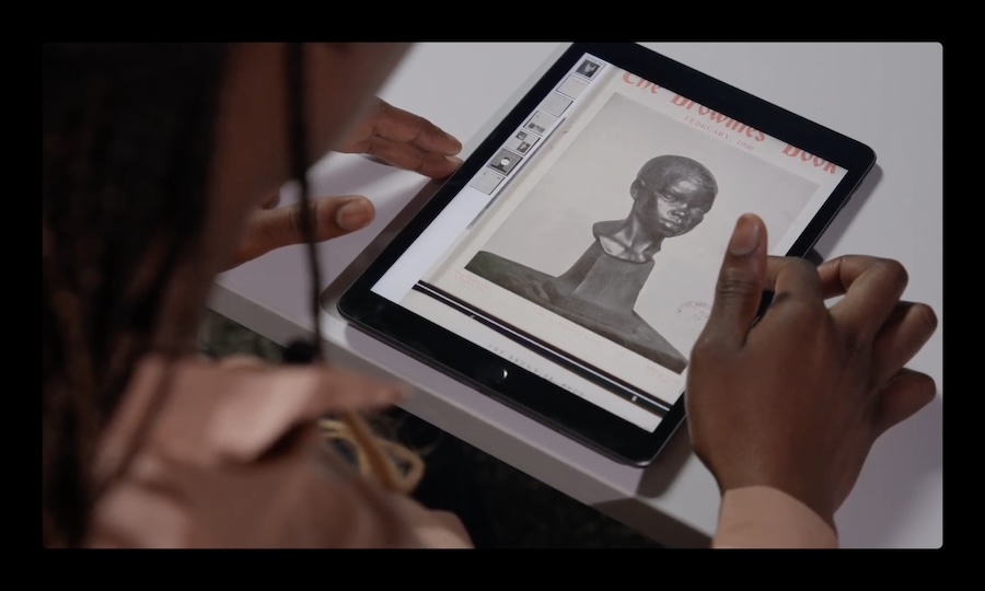 an image over the shoulder of Kadiatou Tubman, only shoulder and hands visible, holding an ipad with an image of a pedestal and head displayed