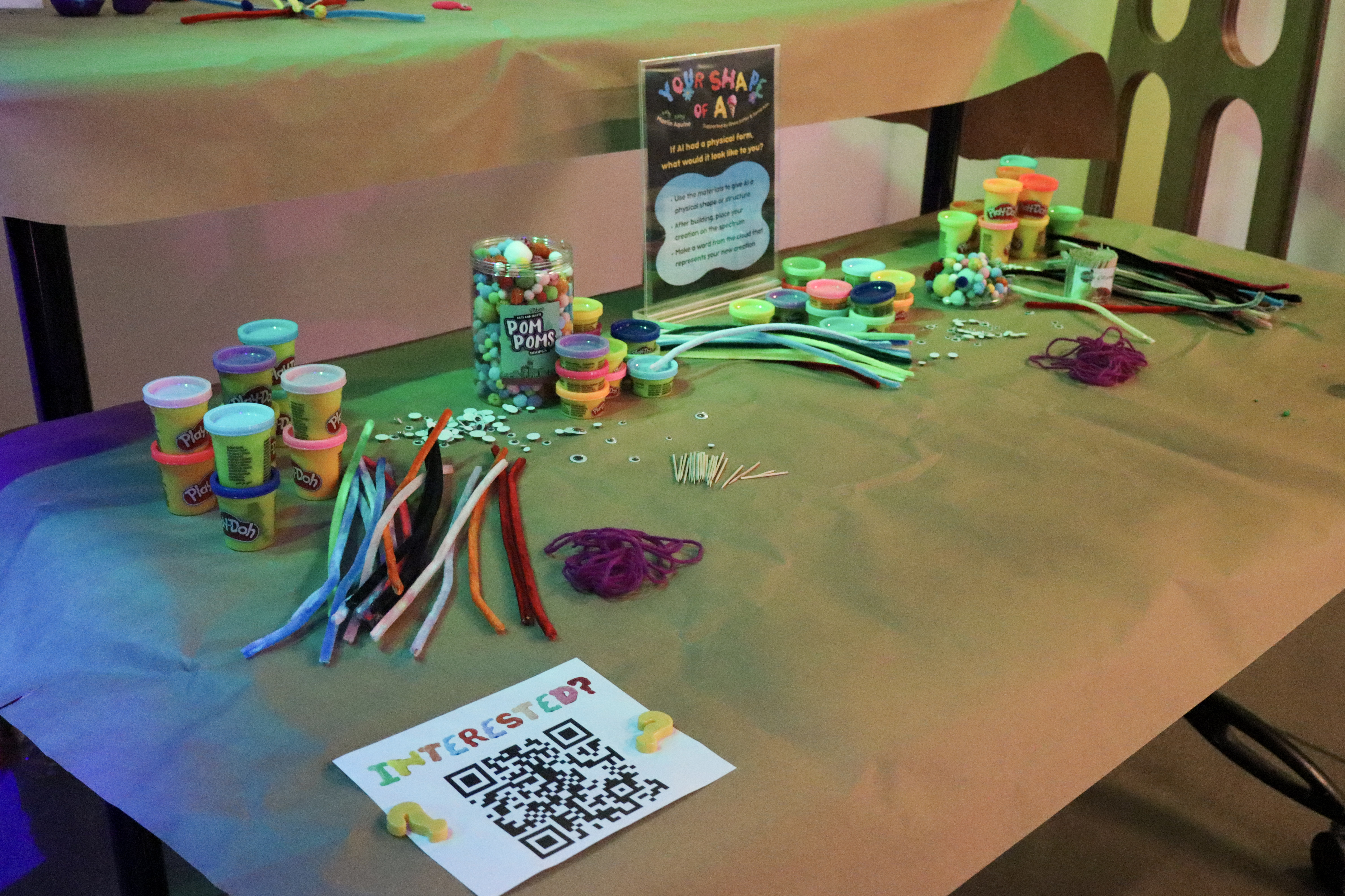 A workstation covered with craft paper with playdough, pipe cleaners, and playful art materials.