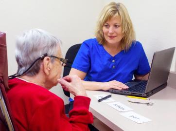 Speech-language clinician seated with an older adult at a table using word cards during a language assessment