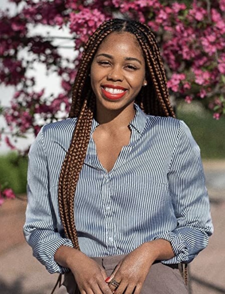 Derecka Purnell standing against a colorful blurred garden smiling