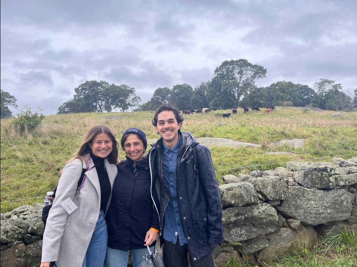 Two women & one man standing in front of pasture with cows
