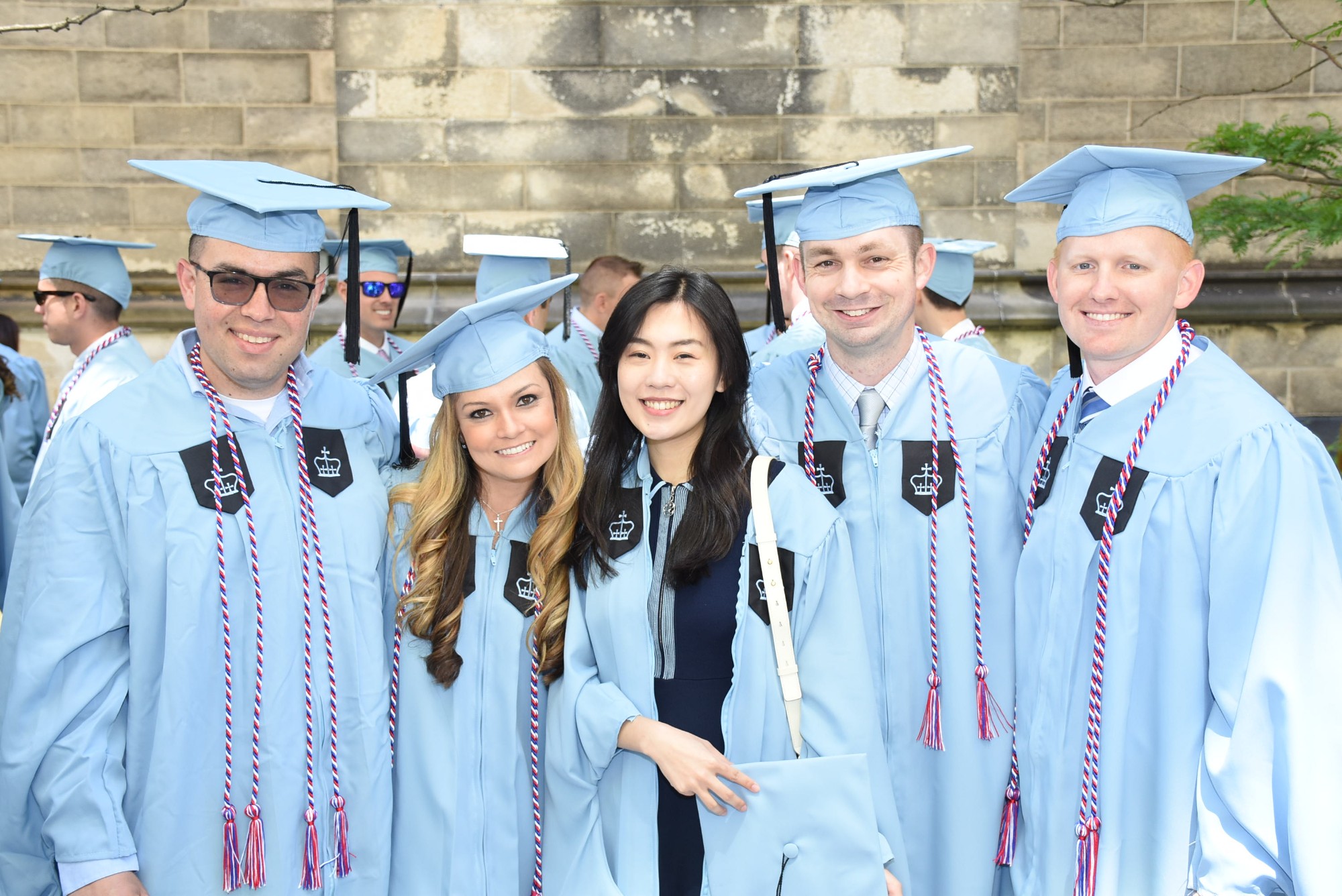 Five ELDP graduates smiling in light blue Columbia graduation gowns.