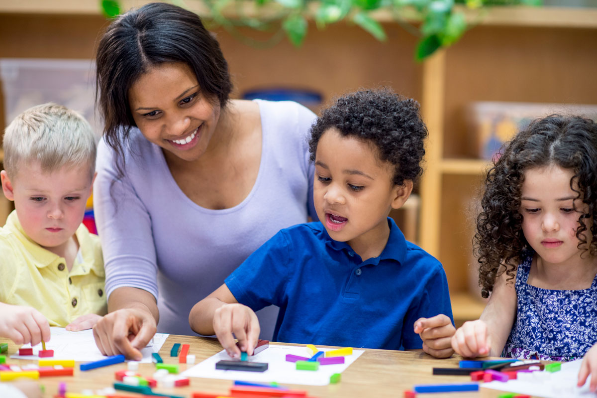 Three pre-school aged children work on a project with their teacher