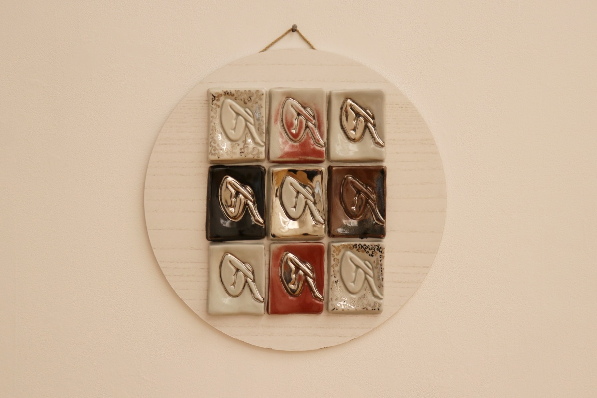 Nine ceramic plaques in different colors, featuring a woman in the fetal position.