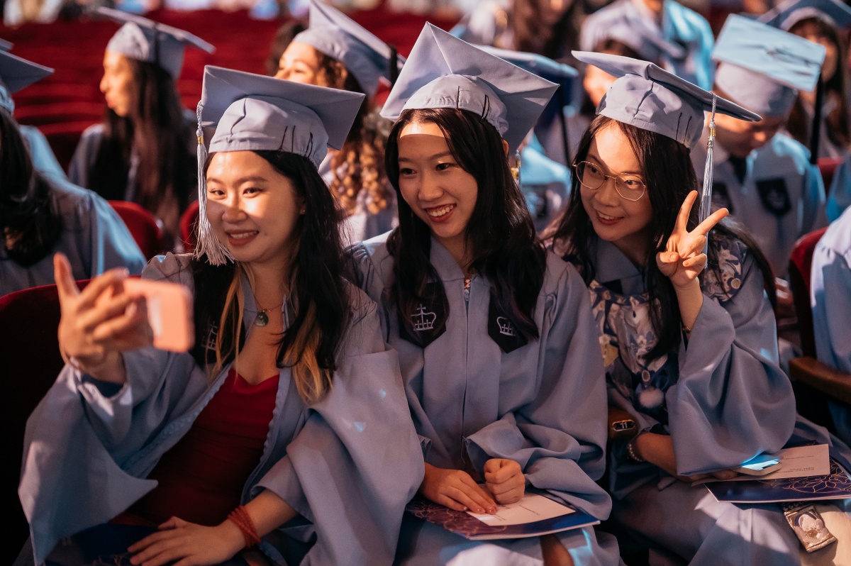 three students in graduation robes take a selfie during Convocation 2024