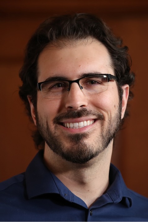 Matt Zajic is smiling. He has dark hair, a beard and is wearing glasses