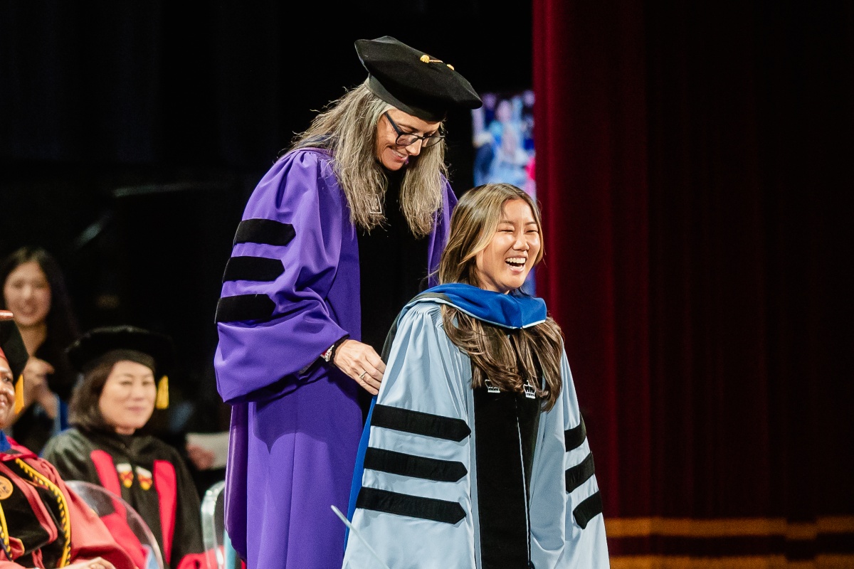 Doctoral graduate receives her hood while smiling.
