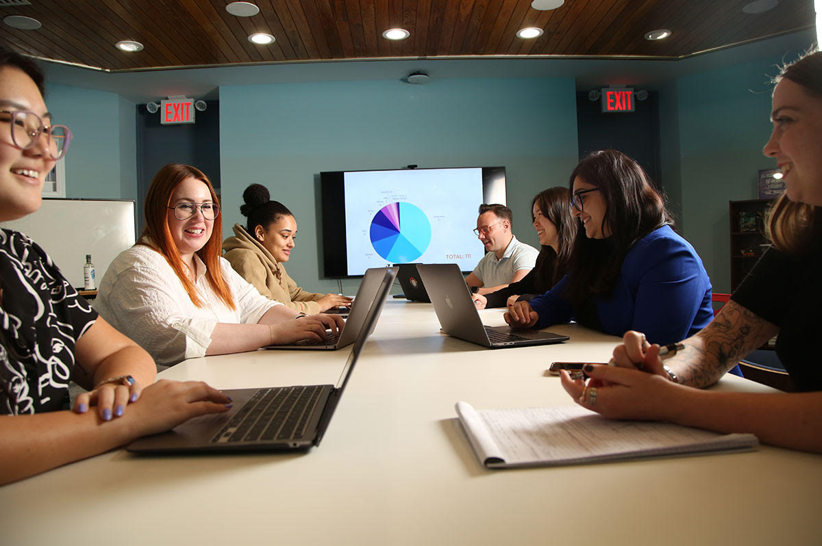 People smiling and sitting at a table with laptops